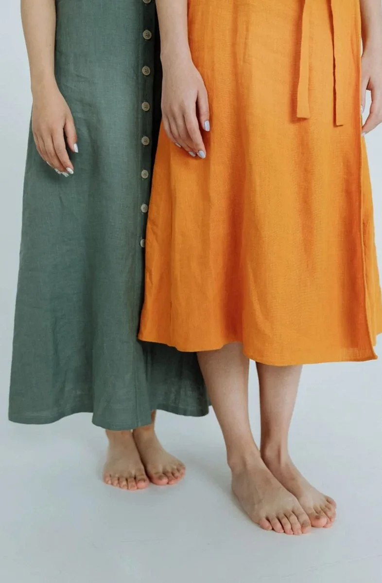 Two women in long green and orange linen skirts, shown from the waist down